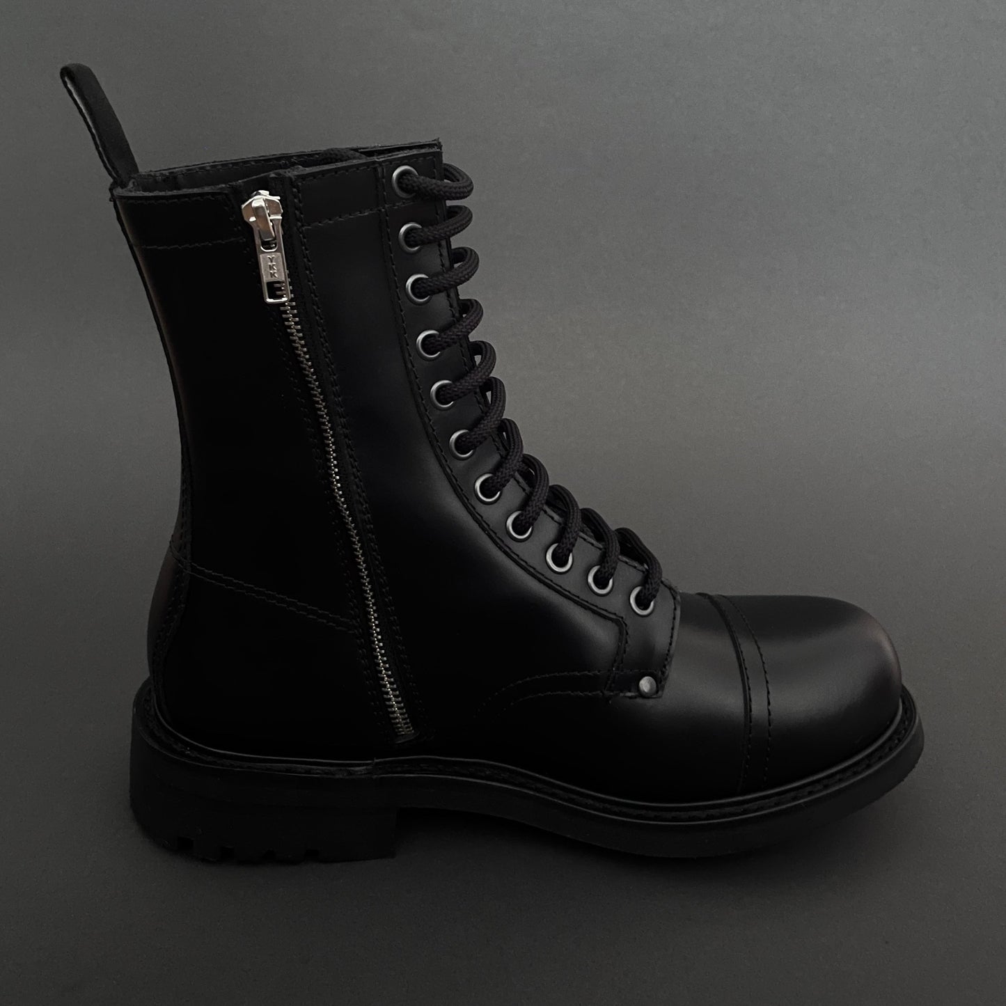 Black leather boot with zipper on a gray background