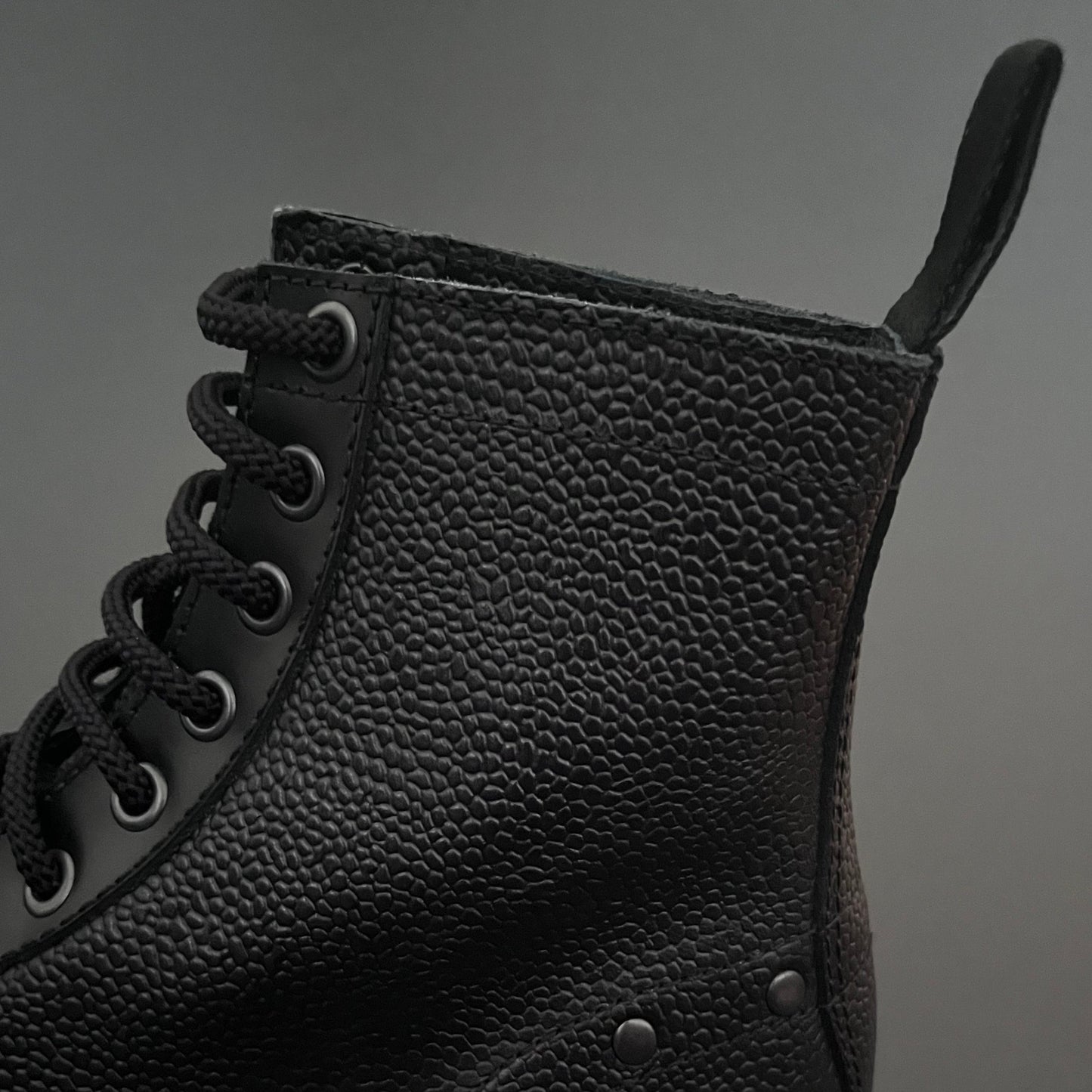 Black leather boot with textured finish on a gray background