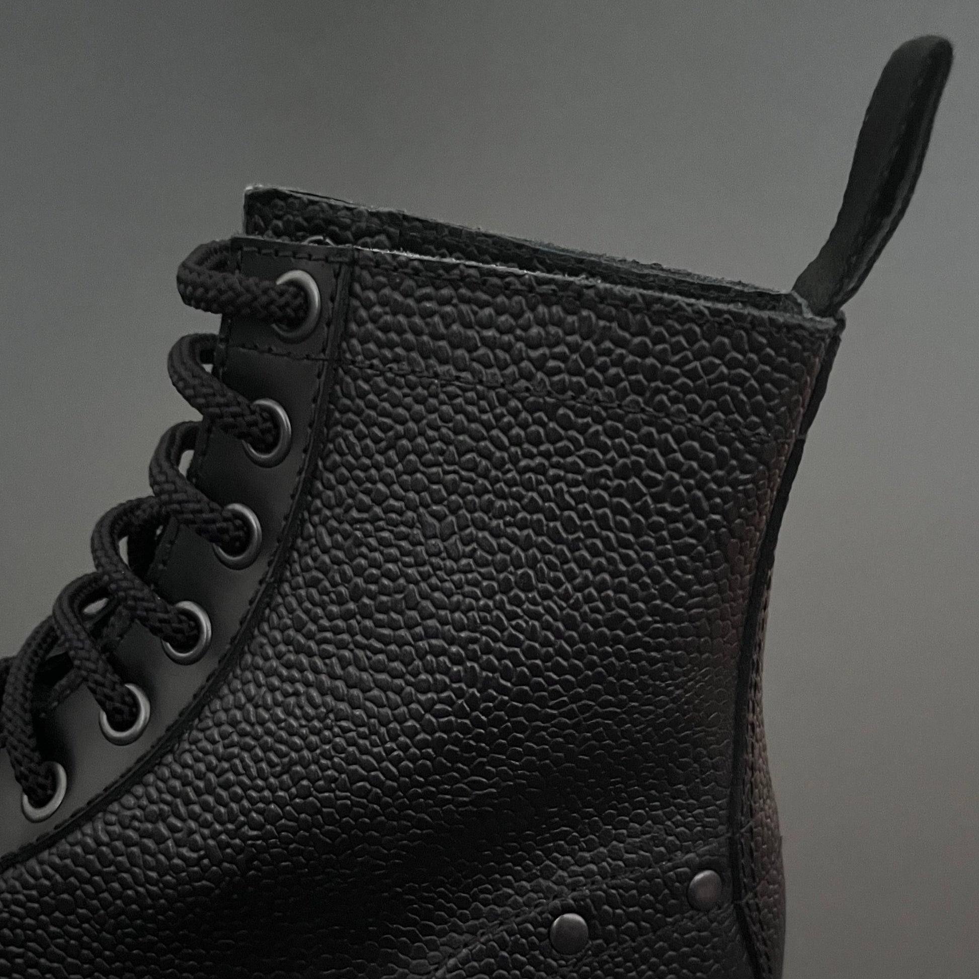 Black leather boot with textured finish on a gray background